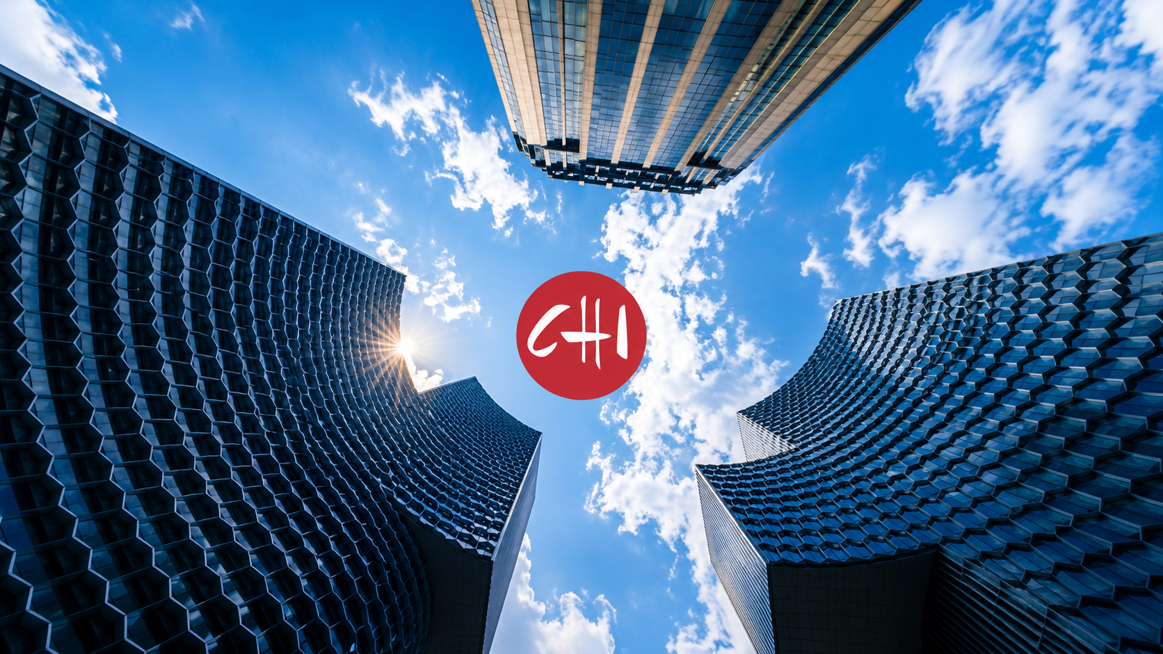 Upward view between three tall buildings toward blue sky with clouds, sun flare, and red CHI circle at center